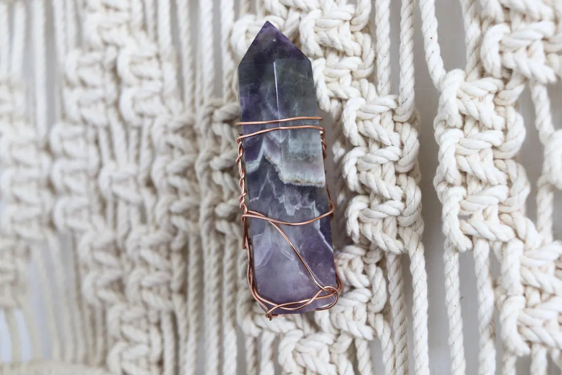 Close-up of a wire-wrapped purple crystal on a handmade macrame drum hanger