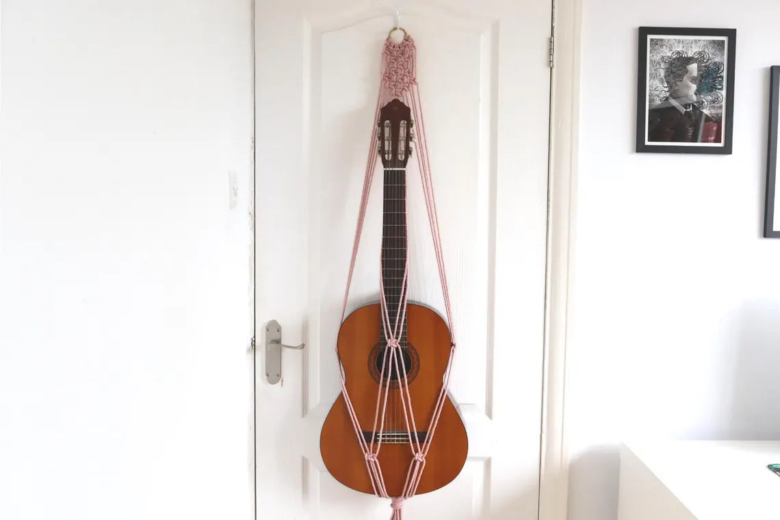 ballet macrame guitar hanger with bamboo hoop holding an acoustic guitar on a wall