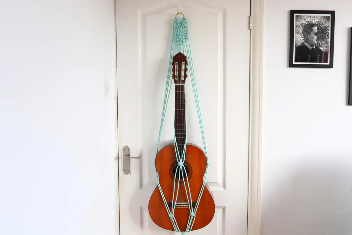 mint macrame guitar hanger with bamboo hoop holding an acoustic guitar on a wall