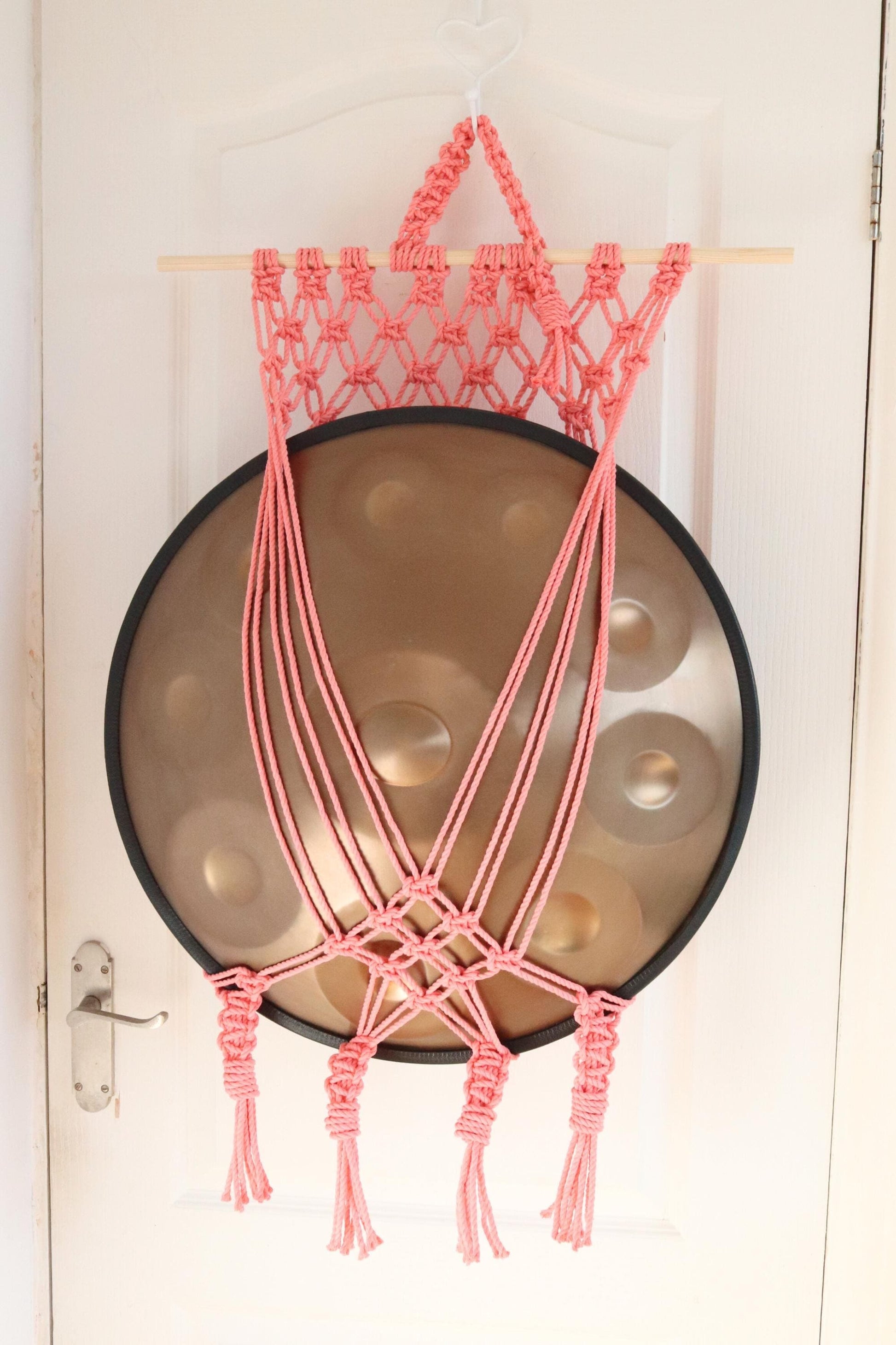 Pink macrame plant hanger hanging on a door with a decorative plate below.