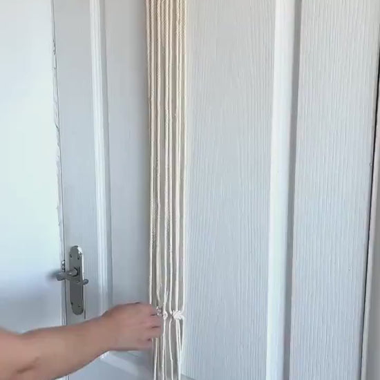 Off-white macrame guitar hanger with bamboo hoop holding an acoustic guitar on a wall