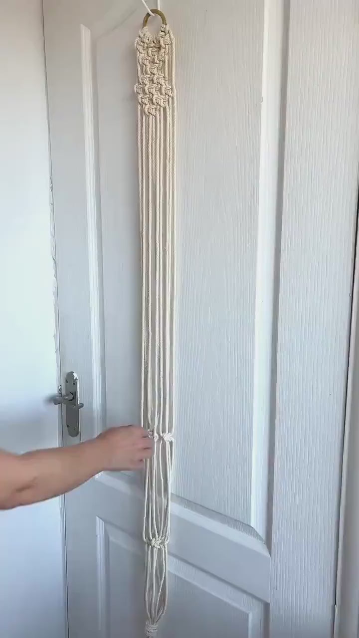Off-white macrame guitar hanger with bamboo hoop holding an acoustic guitar on a wall